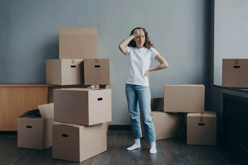 Tired upset woman standing with cardboard boxes in empty room. Eviction, divorce, hard moving day